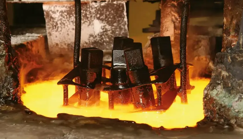 Metalowe elementy zanurzane w rozgrzanym płynie, proces hartowania. Para unosi się wokół.