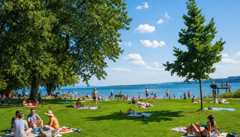 Sonniger Tag im Strandbad Bodensee. Menschen entspannen auf Decken im Gras, baden im See und genießen die Aussicht.