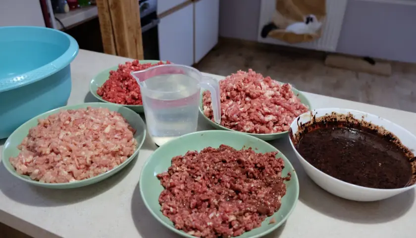 Przygotowania do zdrowej diety BARF dla kota: mielone mięso w miseczkach, dzbanek z wodą i ciemna masa.