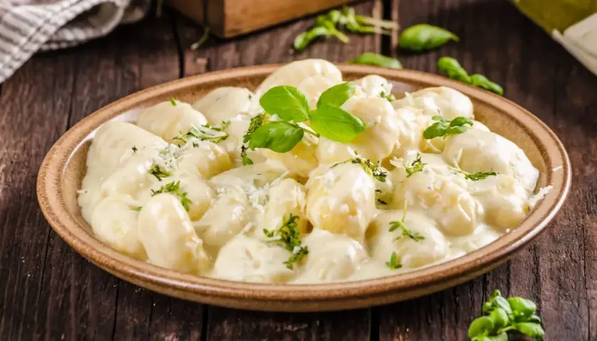 Pyszne gnocchi z kurczakiem w kremowym sosie, udekorowane bazylią i parmezanem, na drewnianym stole.