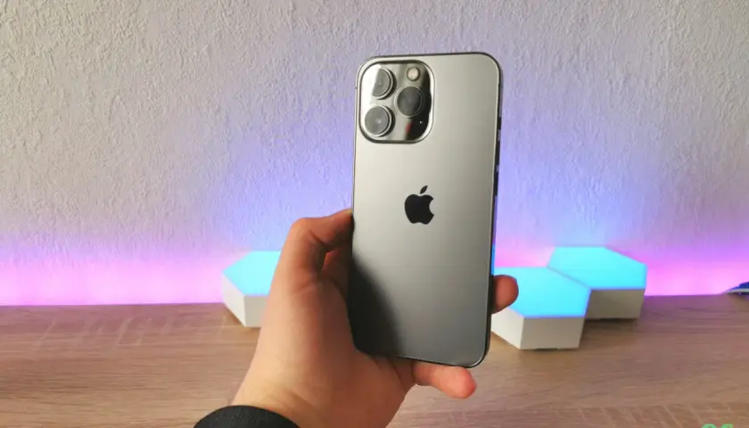 Dłoń trzyma szary iPhone 13 Pro z potrójnym aparatem. Wymiary telefonu idealnie pasują do dłoni.