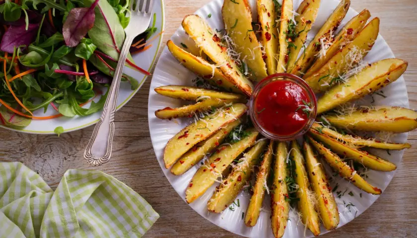 Pieczone ziemniaki w kształcie łódeczek, posypane serem i ziołami, podane z ketchupem. Idealna posypka do ziemniaków!
