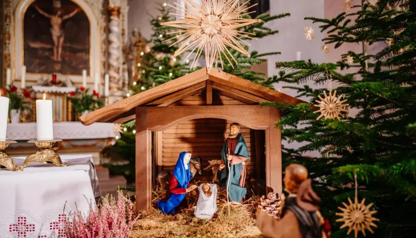 Krippe in einer Kirche, die zeigt, was ist Weihnachten: Maria, Josef und das Jesuskind. Weihnachtsbäume und Kerzen schmücken den Altarraum.