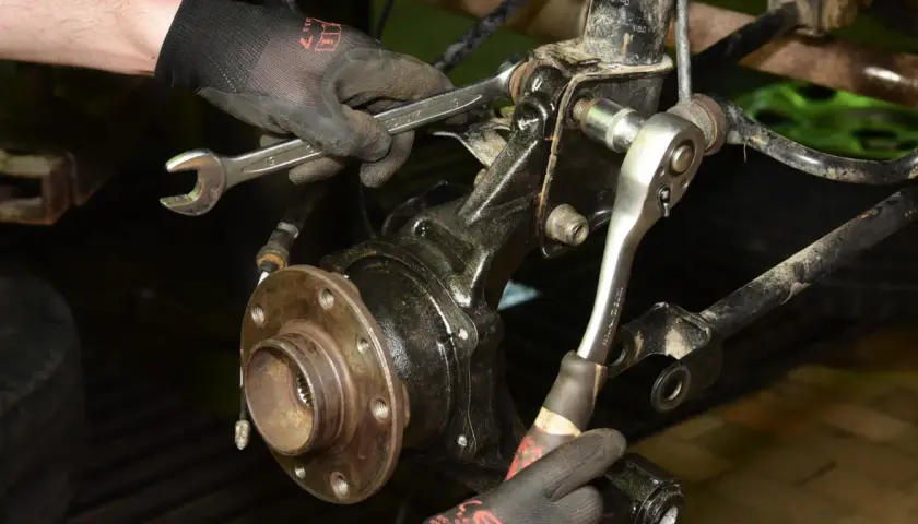 Mechanik w rękawiczkach dokonuje wymiany łożyska koła, używając kluczy do odkręcenia elementów zawieszenia.