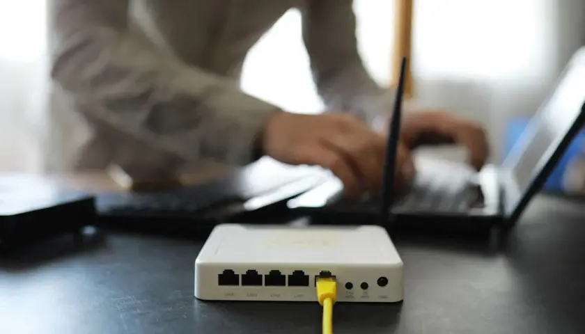 Connexion internet : faut il mettre les espaces pour la clé wifi ? Un routeur blanc est branché, une personne tape sur un ordinateur portable.