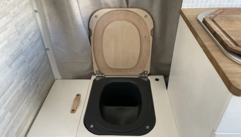 WC de camping aménagé avec abattant en bois et cuvette noire.