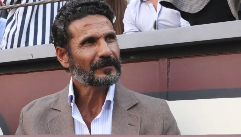 Un torero y actor español, con barba canosa y mirada intensa, viste chaqueta de lino y camisa a rayas.