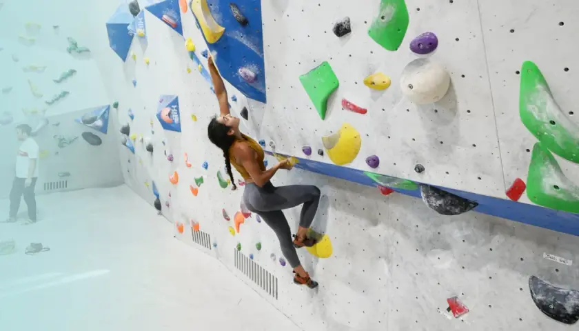 Eine Frau klettert an einer Boulderwand. Das zeigt, was ist bouldern: eine Herausforderung für Kraft und Geschicklichkeit.