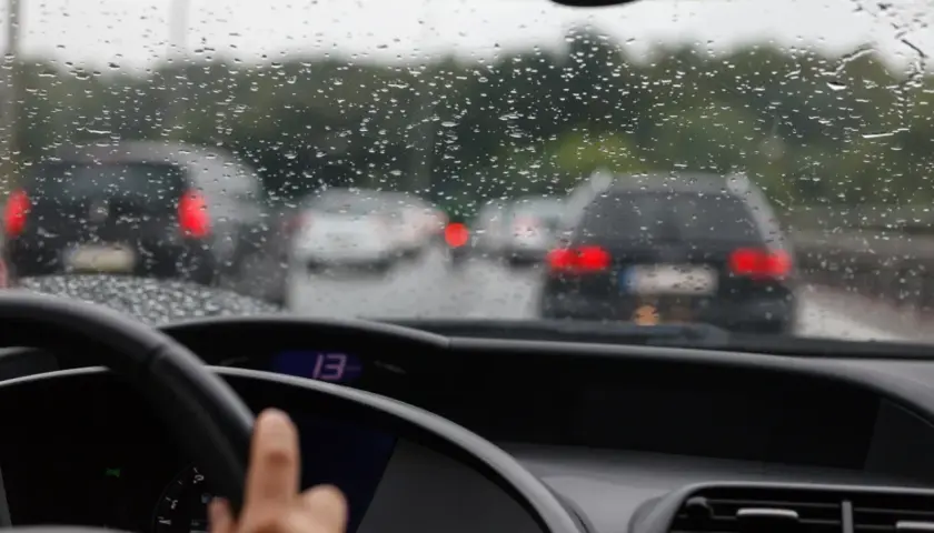 Widok z wnętrza samochodu na deszczową drogę z innymi autami i kroplami na szybie.