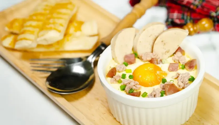 Un œuf cocotte bain-marie, garni de saucisse et de viande hachée, servi avec des bâtonnets de pain grillé.