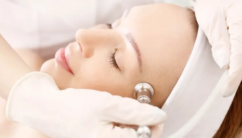 Zabieg oxybrazji na twarz. Kosmetolog w rękawiczce wykonuje delikatny peeling skóry.