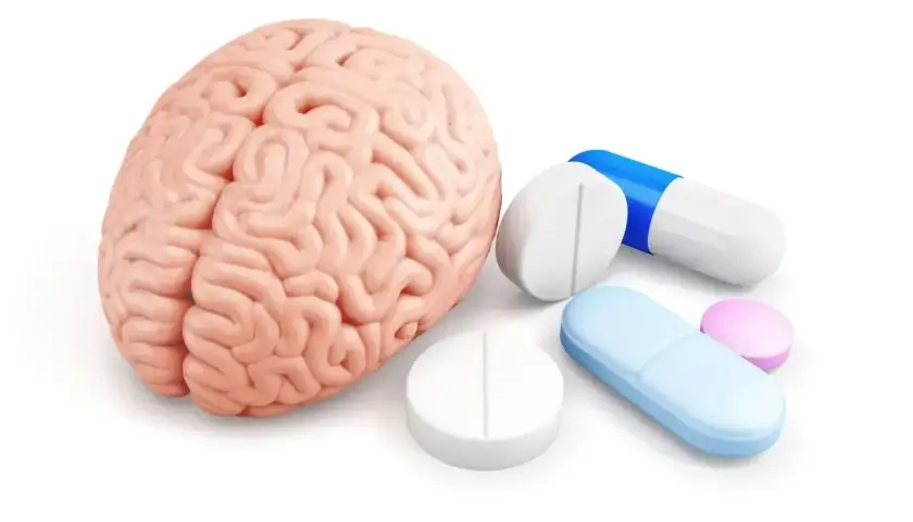 Model ludzkiego mózgu obok tabletek i kapsułek, sugerujące leczenie psychotropowe.