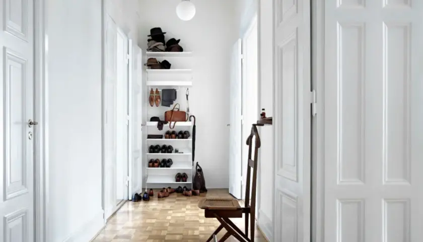 Langer schmaler Flur Ideen: Weißer Regal mit Hüten, Schuhen und Tasche. Holzboden, weiße Türen, Stuhl.