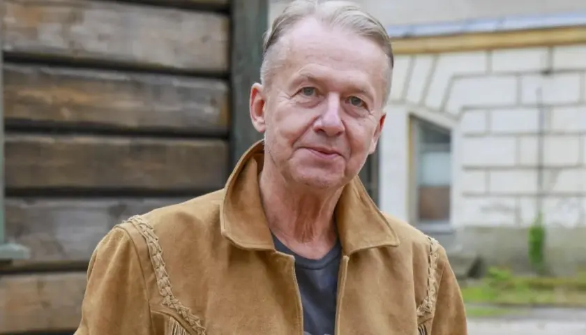 Bogusław Linda w brązowej kurtce z zamszu, z frędzlami i ozdobnymi szwami.