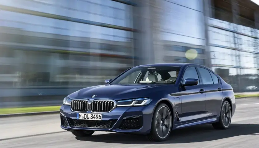 Granatowe BMW G30 540i sunie po drodze, odbijając się w nowoczesnej architekturze.