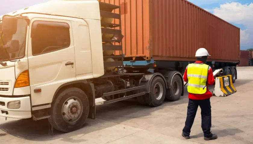 Ein Mann in Warnweste prüft Dokumente neben einem LKW mit Container. Alles bereit für den Frachttransportvertrag.