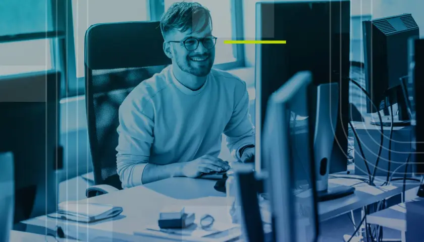 Un homme souriant travaille sur son application bureau, entouré d'écrans d'ordinateur dans un espace moderne.