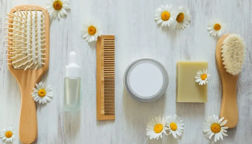 Cepillo, peine, jabón y serum de cuidado personal, todo cruelty free, rodeado de margaritas sobre fondo de madera.