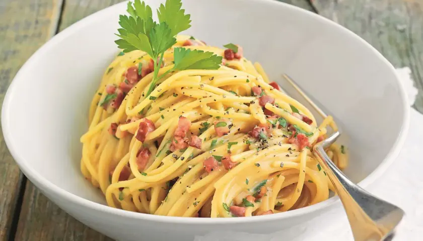 Ein Teller Spaghetti mit cremiger Sauce, Speckwürfeln und Petersilie. Ein Klassiker: Schinken Carbonara.