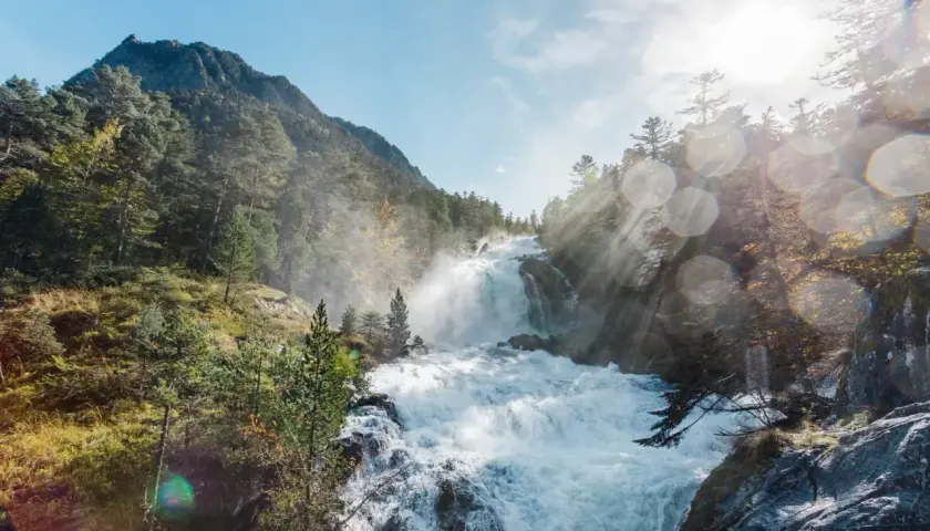 Cascada rugiente en un bosque de montaña, con rayos de sol atravesando la bruma. Un paisaje espectacular que evoca la fuerza de la naturaleza en el **pont de espagne**.