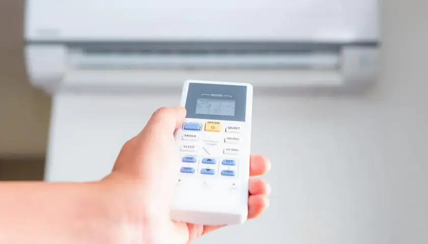 Mano sujetando control remoto de aire acondicionado, ajustando el modo calor a 25 grados.