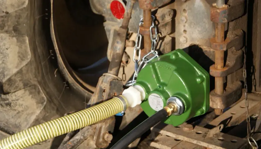 Grüne Zapfwellenpumpe mit Schläuchen an einem Traktor.