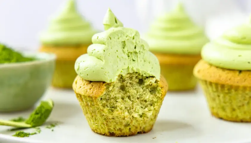 Saftige matcha cupcakes mit leuchtend grünem Topping. Ein Bissen fehlt, um die zarte Textur zu enthüllen.