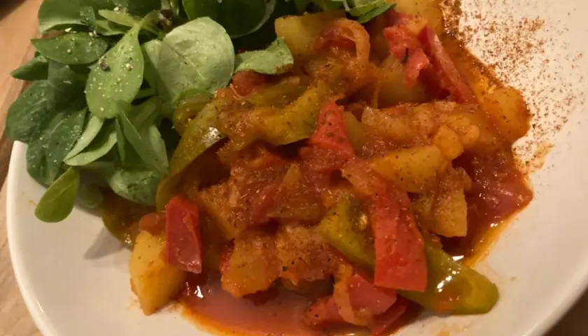 Un plat coloré de poivrons et pommes de terre mijotés, servi avec une salade verte. Une recette simple et savoureuse.