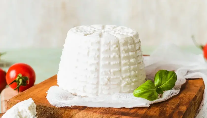 Świeża ricotta na desce, obok pomidorki i bazylia. Idealny składnik do lekkich dań.