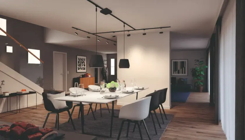 Nowoczesny salon z jadalnią, gdzie centralnym punktem jest stół z krzesłami, a nad nim elegancki system oświetlenia szynowego.