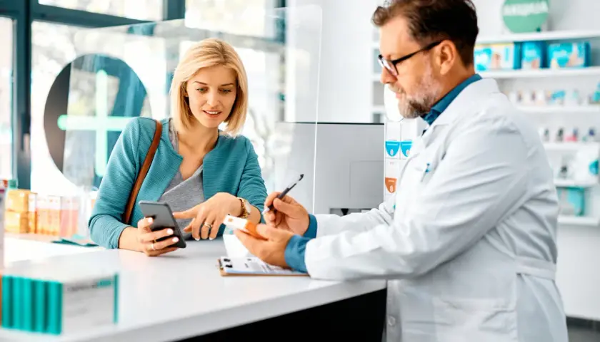 Farmacista spiega a cliente un esempio di farmaci off-label, mostrando una scatola e consultando il telefono.