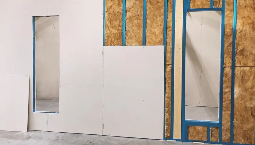 Fase iniziale di come fare una parete in cartongesso: pannelli bianchi fissati su struttura metallica blu, con isolamento visibile.