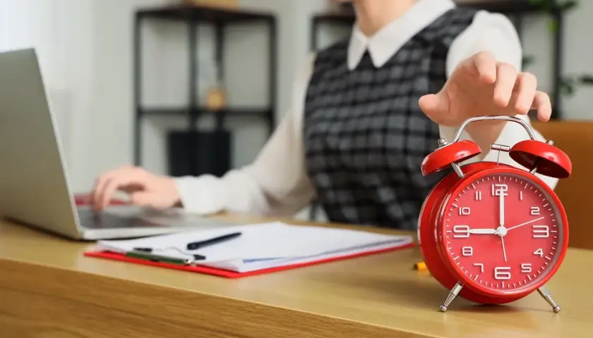 Kobieta wyłącza budzik, pracując przy laptopie. Czyżby to początek dnia w modelu 4 dniowy tydzień pracy?