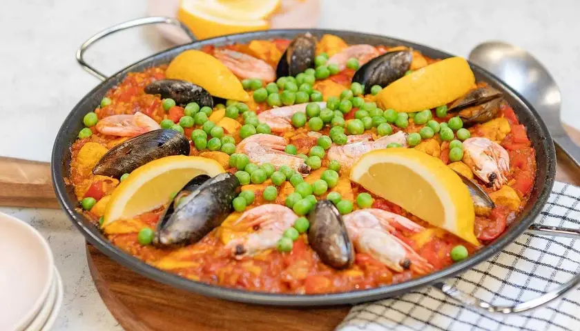En stor paella med räkor, musslor, gröna ärtor och citronklyftor. Perfekt för ett somrigt paella recept.