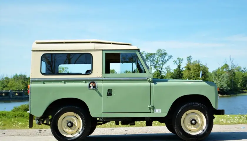 Land Rover Santana verde y crema, listo para una aventura todoterreno junto a un lago.