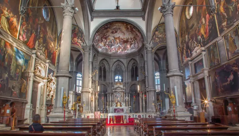 Intérieur de San Zaccaria à Venise, avec des fresques grandioses, des colonnes imposantes et des bancs en bois.