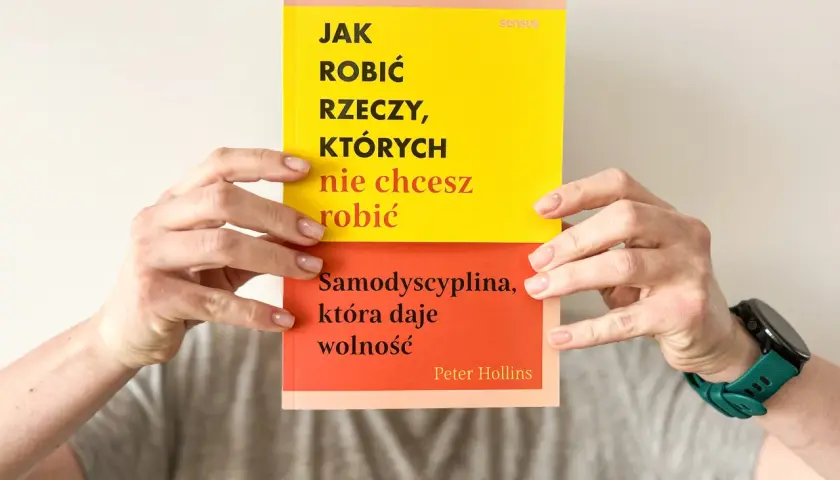Dwie ręce trzymają książkę "Jak robić rzeczy, których nie chcesz robić". Na okładce hasło: "Samodyscyplina, która daje wolność".