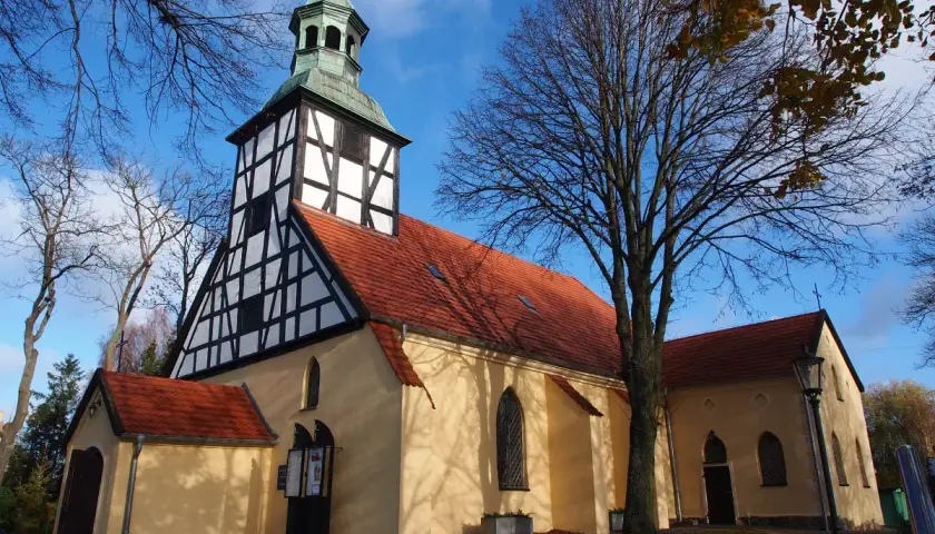 Piękny kościół w Łebie z charakterystyczną wieżą o konstrukcji szachulcowej, otoczony jesienną zielenią.