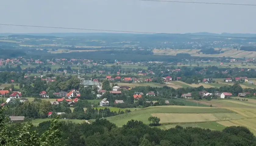Widok na malowniczą wieś Przytkowice z kościołem w centrum, otoczoną zielonymi wzgórzami i polami.