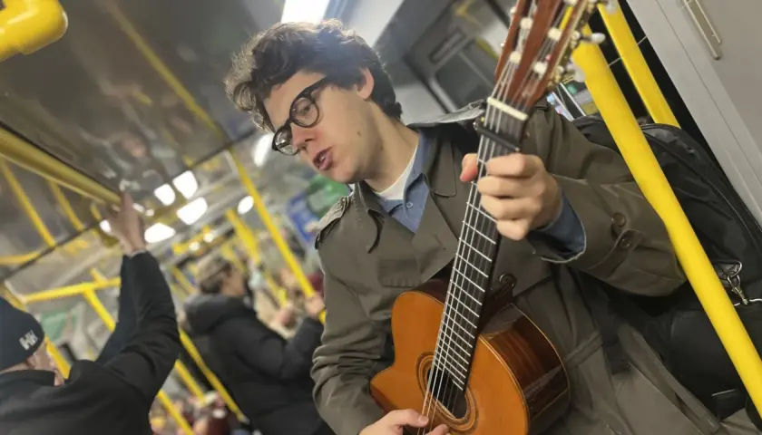 En ung man med glasögon spelar gitarr på tunnelbanan, en musikalisk själ med stockholm roots.