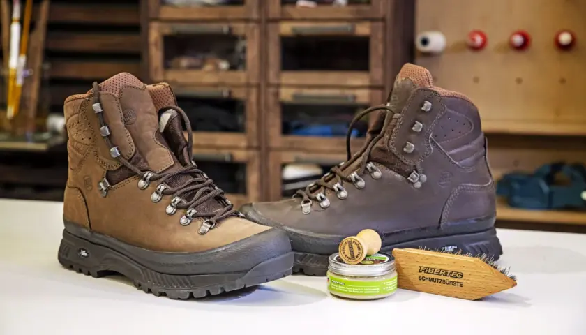 Zwei braune Wanderschuhe bereit zum Reinigen, daneben eine Dose Wachs und eine Bürste.
