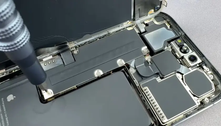 Naprawa telefonu z powodu słabej baterii w telefonie. Wkrętak odkręca śrubkę przy baterii.