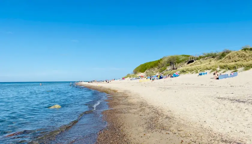Sonniger Tag am Strand Nonnevitz. Menschen entspannen sich unter bunten Schirmen, während sanfte Wellen das Ufer erreichen.