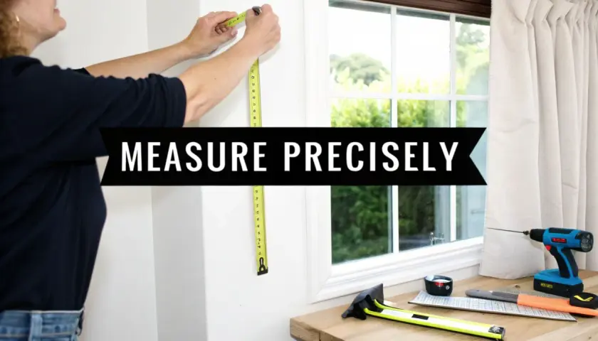 A person measures a window frame, demonstrating how to measure for pinch pleat curtains. Tools are laid out on a wooden surface.