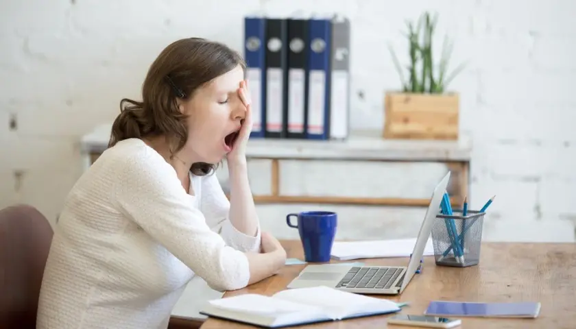 Donna al lavoro, con sbadigli continui, forse per l'ansia o la stanchezza. Sul tavolo, laptop, tazza blu e quaderni.