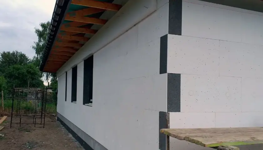 Budowa domu: biały styropian, siatka, klej i cena robocizny. Widać fragmenty ścian, okna i dach.
