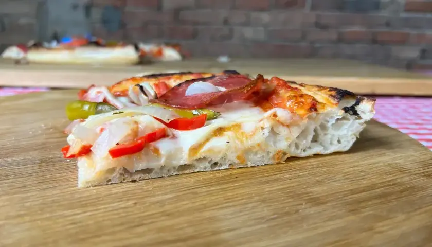 Ein Stück Pizza mit original italienischem Pizzateig Rezept Blech, belegt mit Salami, Paprika und Zwiebeln.