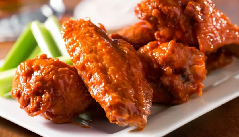 Un plato de alitas de pollo bañadas en salsa picante, acompañadas de bastones de apio fresco. ¡Un clásico irresistible!