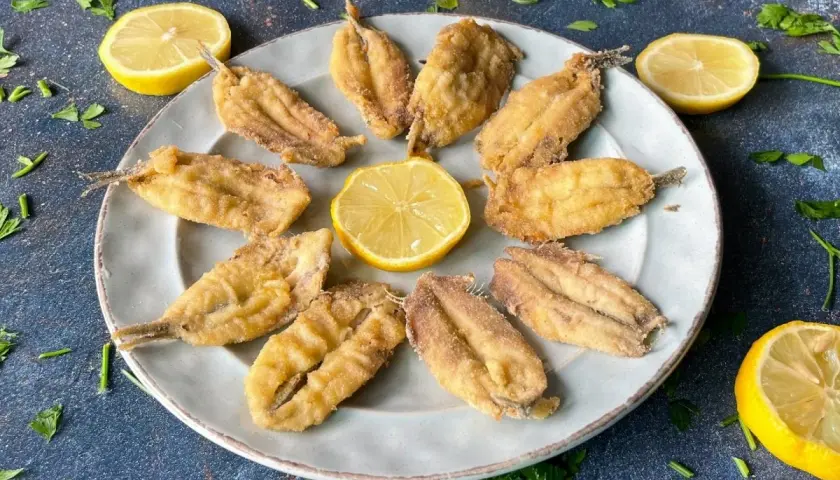 Bocartes fritos crujientes y dorados, servidos en un plato con rodajas de limón y perejil fresco. ¡Un manjar listo para disfrutar!