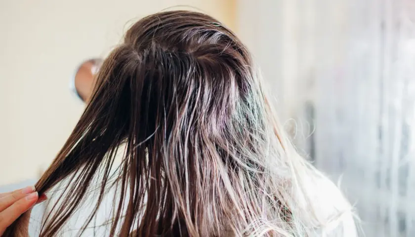 Nasse, braune Haare werden von einer Hand gehalten. Die Frau wäscht ihre **Haare nur mit Wasser**, um sie zu reinigen.